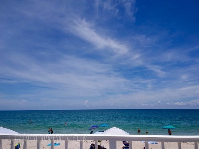 Beach scene With Blue Umbrellas And Beachgoers On Beautiful Blue Sky Day With Wispy Clouds