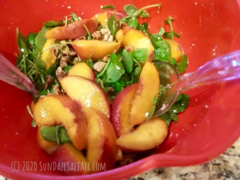 Watercress And Sauteed Peach Salad Being Tossed in Coral Bowl