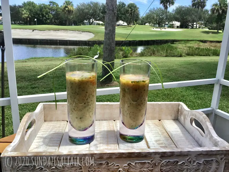 Watercress And Zucchini Soup With Smoked Paprika And Chives In Glasses On Tray Outside With White Bird In the Background