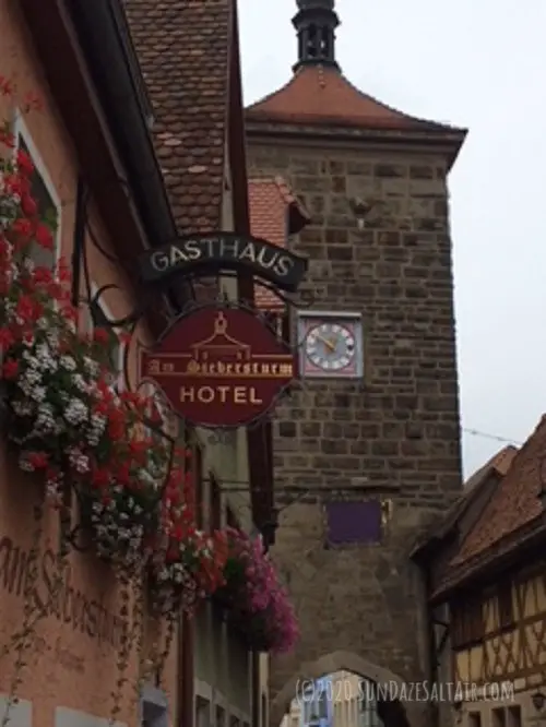 Quaint German window boxes with flowers next to shop signs against backdrop of old medieval brick clock tower