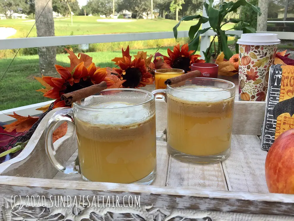 Easy, Delicious Homemade Hot Spiced Caramel Apple Cider In Glass Mugs Surrounded By Beautiful Lake And Fall Decor