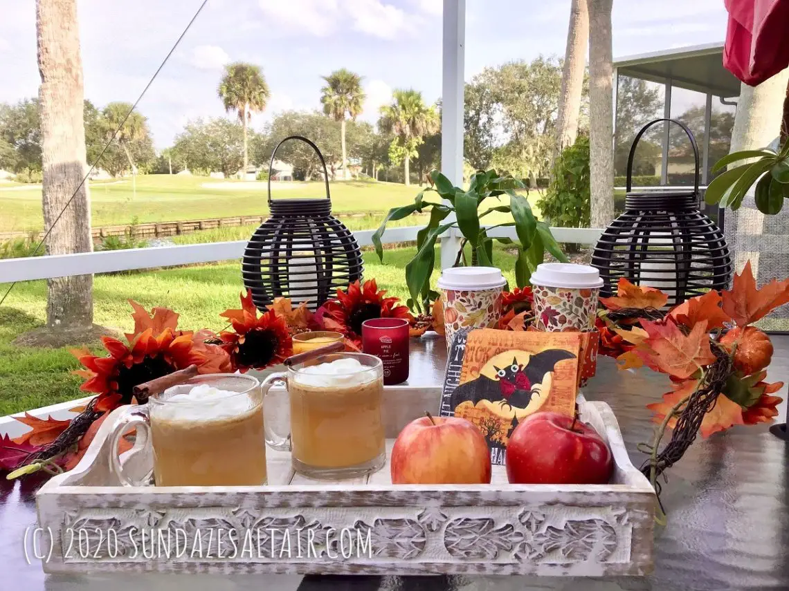 Homemade Warm Caramel Apple Cider Like Starbucks On Wooden Tray Surrounded By Fall Garland Overlooking Beautiful Lake And Scenery