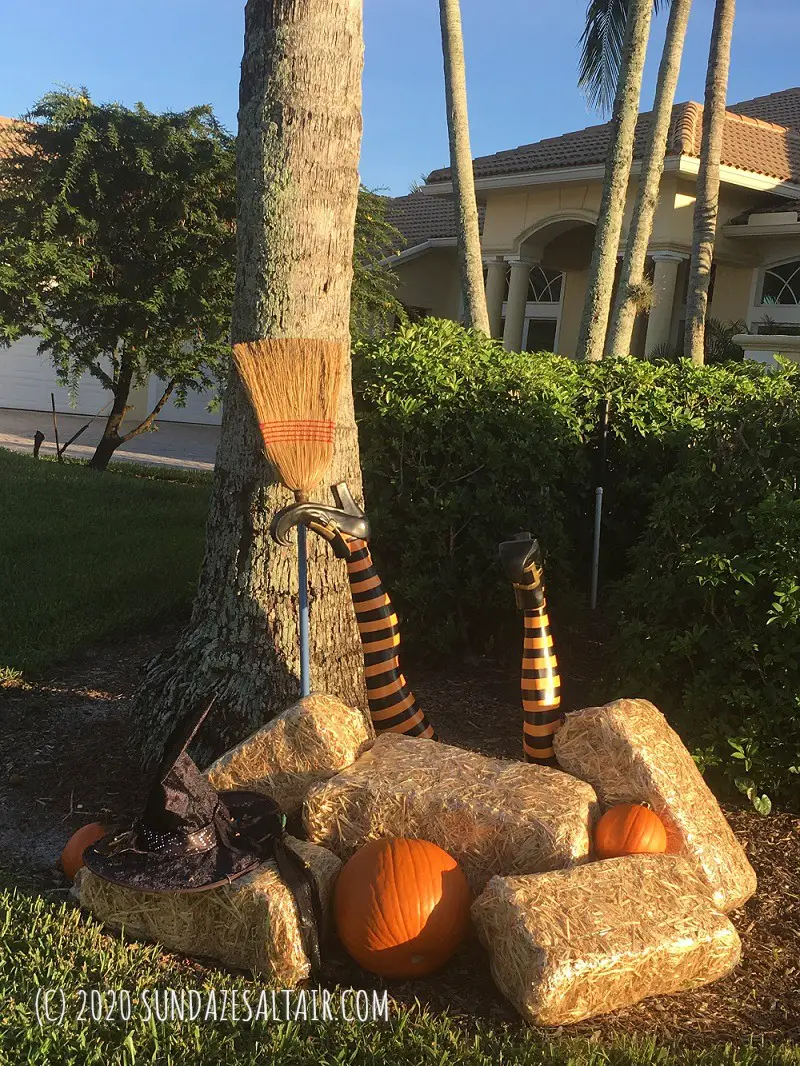 Upside down witch legs yard sticks Halloween decor on hay bales with broom, witch hat and pumpkins