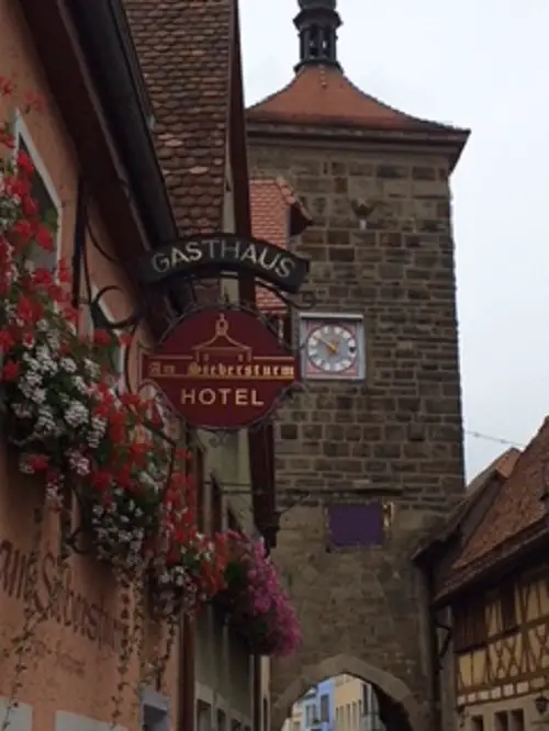 Quaint German window boxes with flowers next to shop signs against backdrop of old medieval brick clock tower