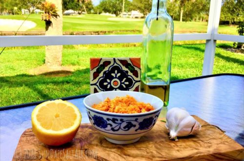 Easiest, Best Hummus Without Tahini - Hummus In Ceramic Dish With Lemon, Olive Oil & Garlic On Wooden Cutting Board Overlooking Lake