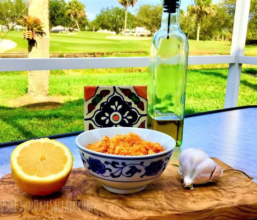 Easiest, Best Hummus Without Tahini - Hummus In Ceramic Dish With Lemon, Olive Oil & Garlic On Wooden Cutting Board Overlooking Lake