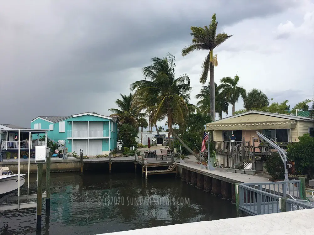 Storm clouds encroach on quaint beach cottages on the water under wind-blown palm trees