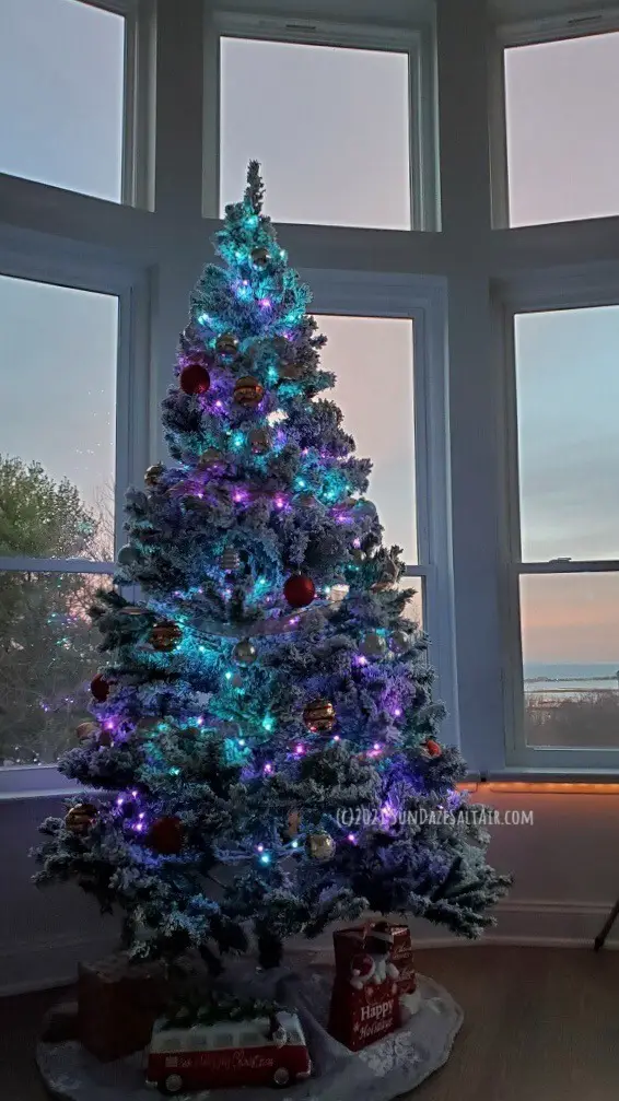 How To Decorate A Room With High Ceilings For Christmas--A flocked Christmas tree with blue & purple lights looks out huge windows to bay